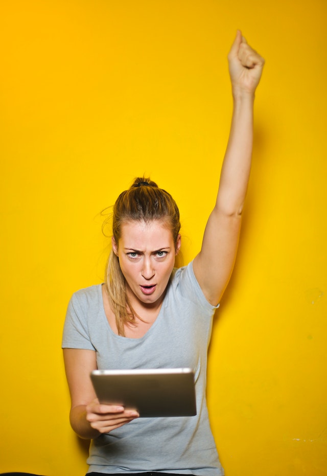 A blonde woman celebrating while holding a tablet device