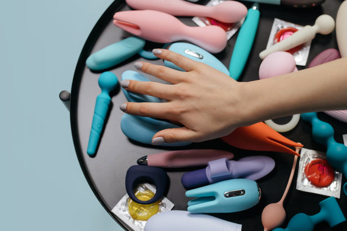 A woman's hand over a selection of sex toys on a table.
