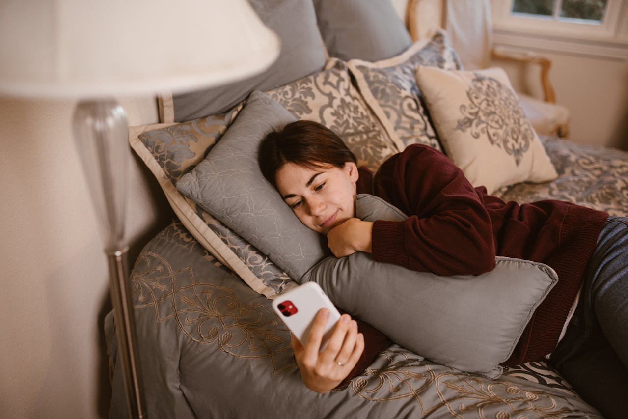 A woman lies on her bed looking at her phone