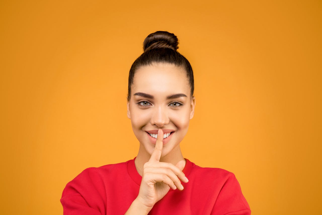 A smiling woman places a finger over her lips in the 'shh' gesture