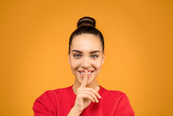 A smiling woman places a finger over her lips in the 'shh' gesture