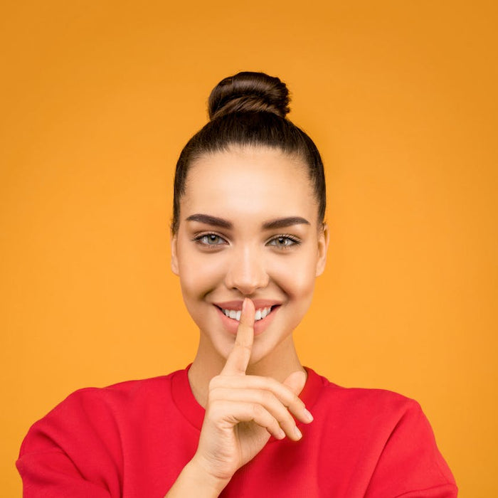 A smiling woman places a finger over her lips in the 'shh' gesture